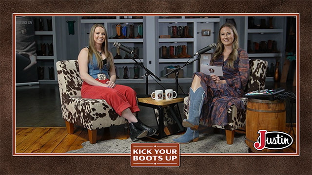 Two women looking at the camera, smiling, sitting, and having a conversation.
